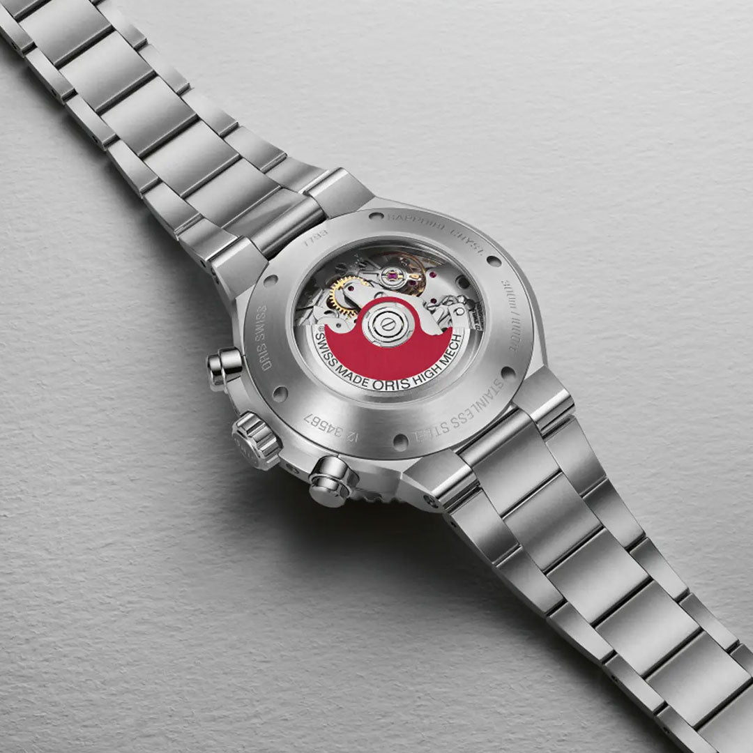 A detailed look at the back of the ORIS Aquis Chronograph Automatic 43.5mm Watch displays its transparent case back, revealing internal gears and a red Swiss-made rotor, all set on a light gray textured surface.