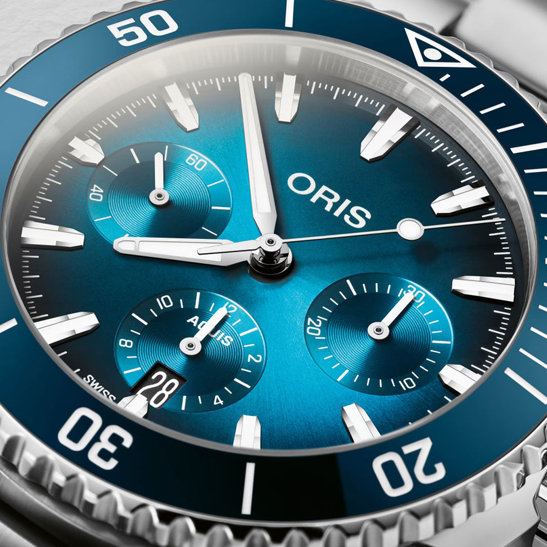 Close-up of the ORIS Aquis Chronograph Automatic 43.5mm Watch featuring a blue dial with three subdials, bold white hour markers, luminous hands, silver bezel, and a date window at 6 o’clock—delivering top toolwatch performance.