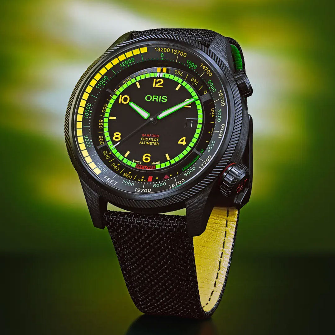 The ORIS Propilot X BWD Limited Edition Automatic Winding 47mm Watch features neon yellow and green dial markings, a black strap with yellow lining, ProPilot Altimeter functions, and is shown against a blurred green background.
