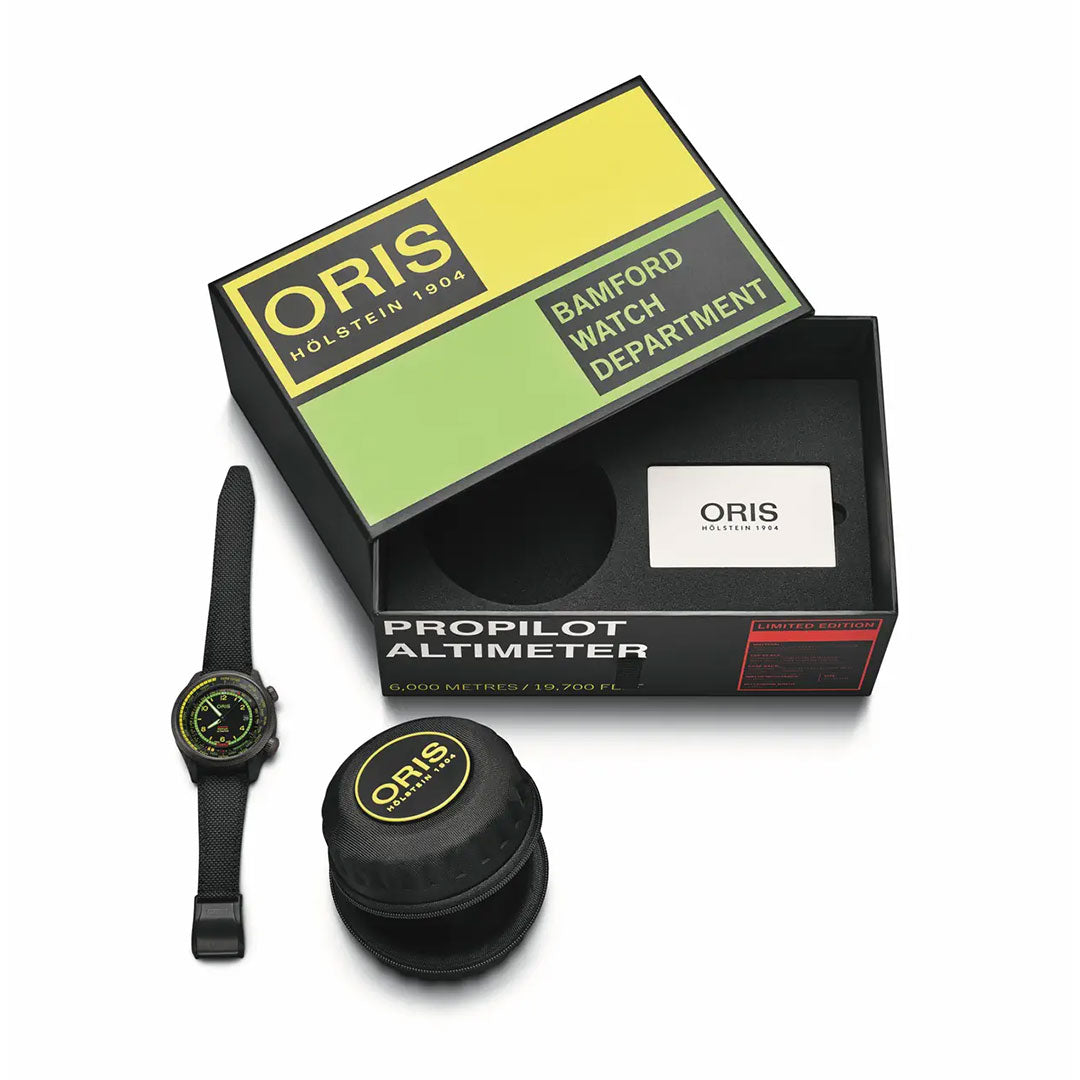 The Oris ProPilot X BWD Limited Edition Automatic 47mm Watch by ORIS is shown with yellow and green accents beside its black and yellow branded box reading "Oris Holstein 1904 Bamford Watch Department" and a round black travel case.