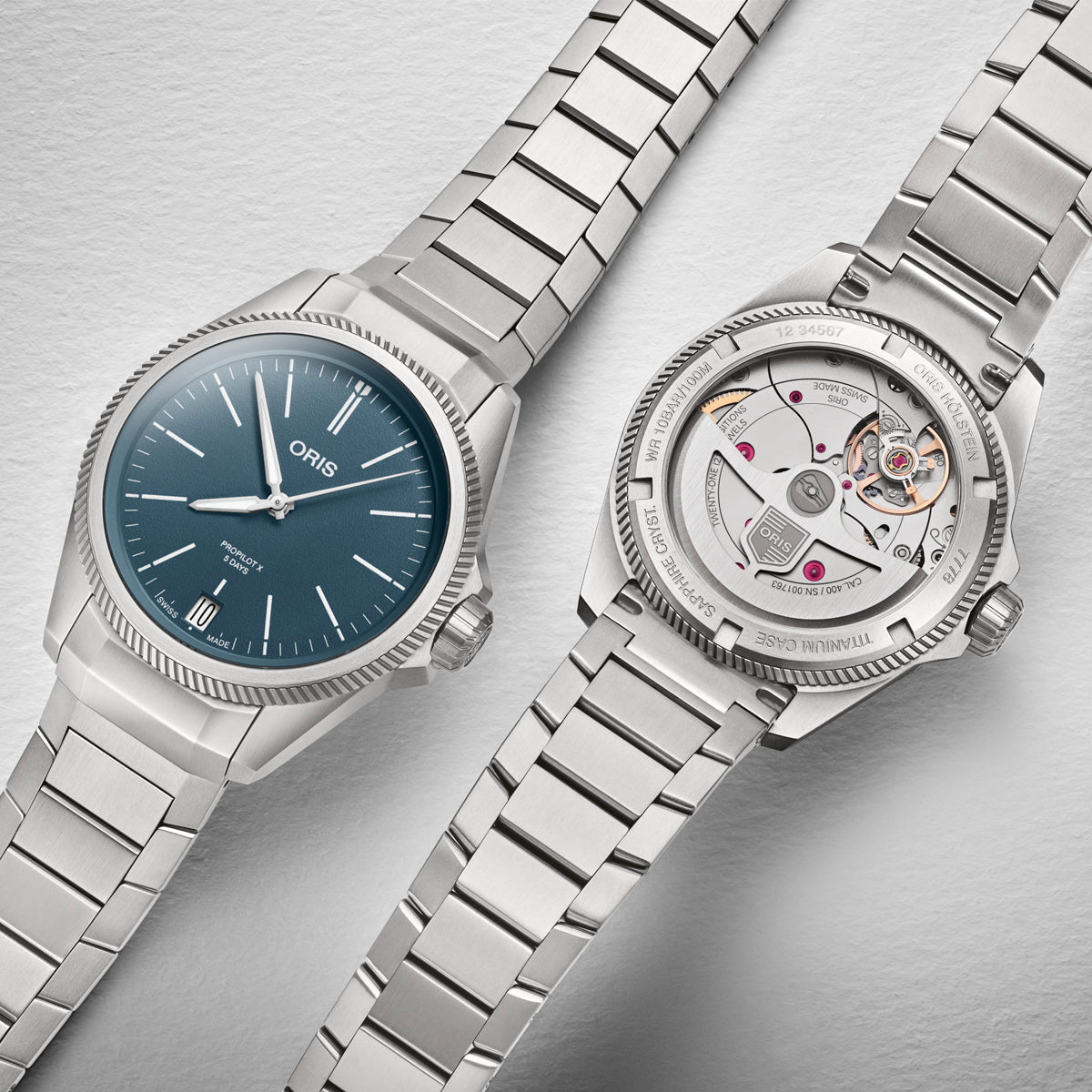 Two wristwatches are placed side by side on a white background. The watch on the left is an Oris Propilot X, showcasing a blue face with silver hour markers and hands. On the right, the Oris Propilot X Calibre 400 Titanium Automatic Winding 39mm Watch reveals its open back, displaying intricate mechanical movements powered by the Calibre 400.