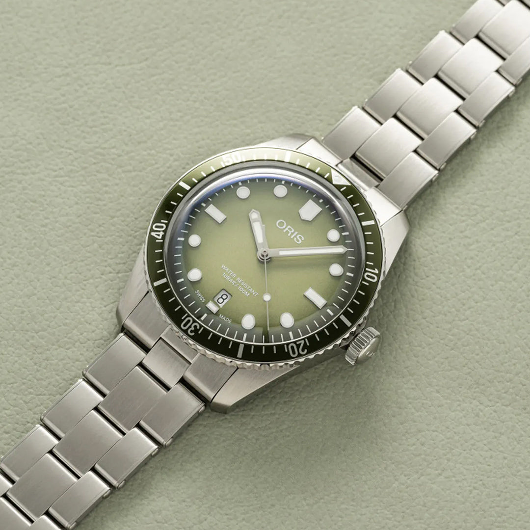 The Oris Divers Sixty-Five Date Automatic Winding 40mm Watch features a green gradient dial with white numerals on a beige textured surface, silver hour markers, a date window, and a black bezel with minute markers. The brand "ORIS" is prominently displayed on the dial.