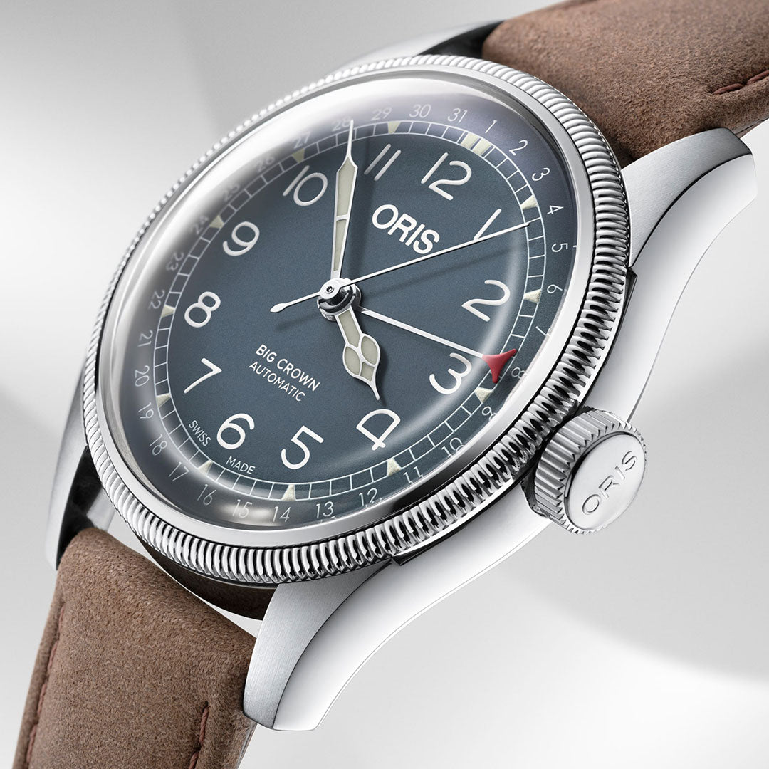 A detailed close-up of the Oris Big Crown Pointer Date Automatic Winding 44mm Watch by ORIS showcases its elegant design. The brown leather strap and silver case frame the watch, while the oversized crown enhances the grey dial with white Arabic numerals and an ornate second hand. The text "Oris Big Crown Automatic" adorns the dial, with an intricately textured bezel accentuating its timeless allure.