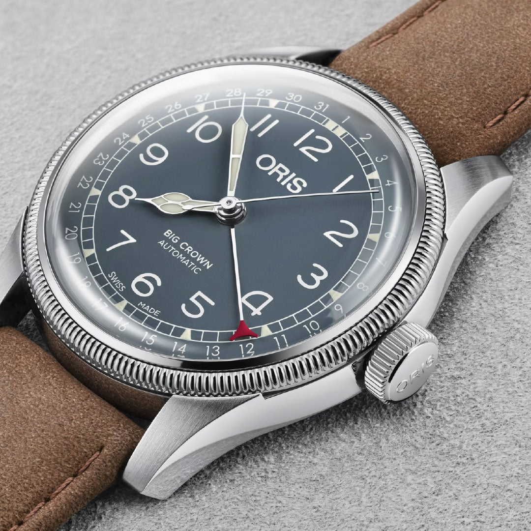 A close-up of the ORIS Big Crown Pointer Date Calibre 754 Automatic Winding 40mm watch, featuring a blue dial, white numerals, red-tipped date hand, and brown leather strap on a light grey textured surface.