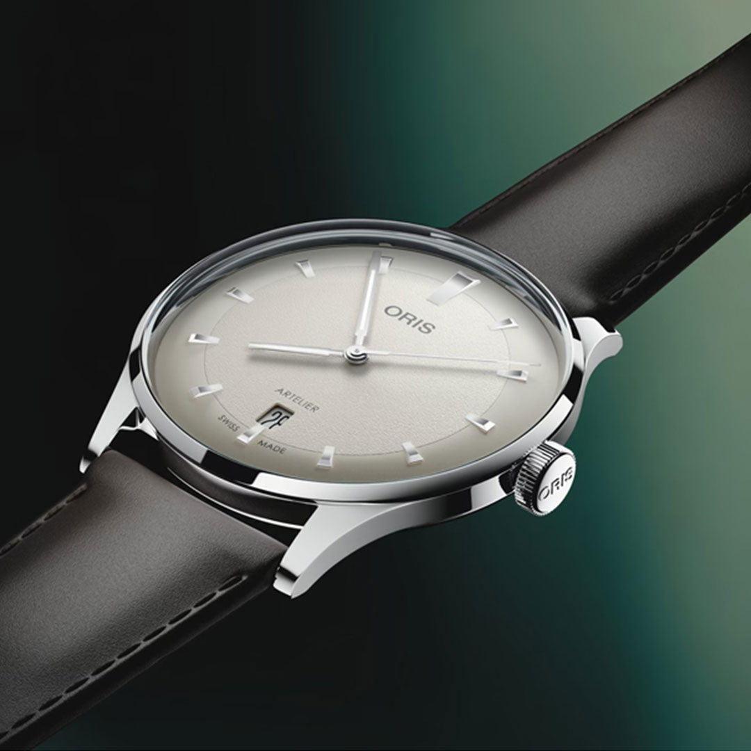 A close-up of the ORIS Artelier Date Calibre 733-1 Automatic 38mm Watch features a silver dial, minimalist markers, and a black leather strap by ORIS, set against a gradient green background.