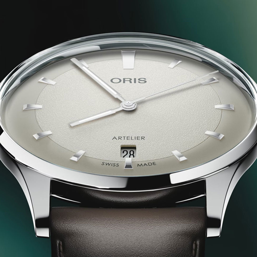 A close-up of the ORIS Artelier Date Calibre 733-1 Automatic 38mm Watch highlights its minimalist beige dial, silver markers and hands, date window at six o’clock, polished silver case, and brown leather strap.