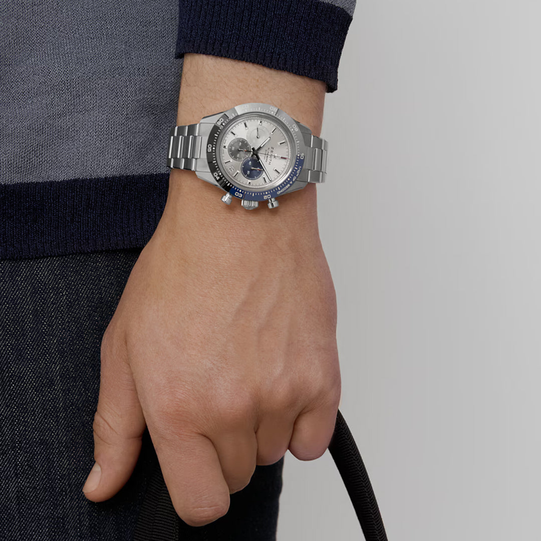 Clad in a dark sweater and jeans, the individual wears a ZENITH Chronomaster Sport El Primero 3600 wristwatch, featuring a detailed face with small dials and a blue-accented bezel. The black strap complements this sophisticated 41mm piece from Zenith's collection.