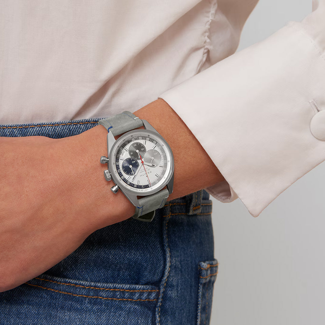 A person in a white shirt and blue jeans is showcasing the ZENITH Chronomaster Original El Primero 3600 38mm Watch. This exquisite piece features a gray strap, round silver case with multiple dials, and is powered by high-frequency chronograph movement from Zenith.