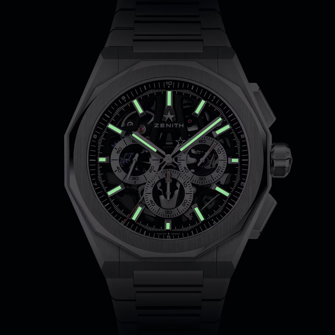 A dark image of the Zenith Defy Skyline Chronograph Skeleton El Primero 3600SK 42mm with a metallic strap. Its modern design showcases luminous green markers and hands on the watch face, multiple detailed subdials, and is powered by the El Primero movement.