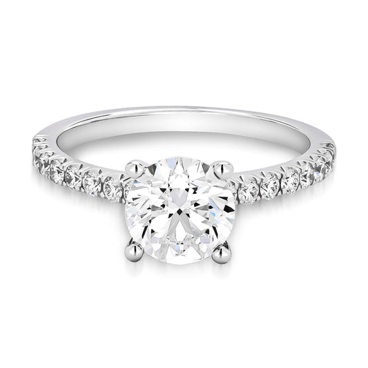 The Raffi&Co® 18K White Gold Round Brilliant Solitaire Diamond Engagement Ring showcases a breathtaking central solitaire diamond, complemented by smaller diamonds elegantly arrayed along the band.