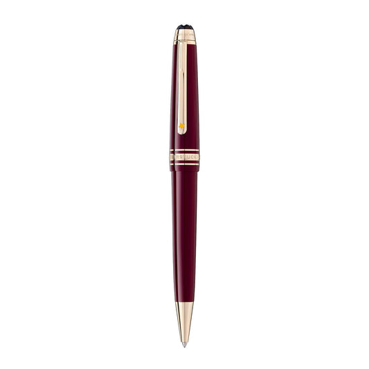 A sleek Montblanc Meisterstück Le Petit Prince Classique ballpoint pen, featuring a burgundy design with gold accents and clip, stands vertically on a white background. The pen is capped and exudes elegance with its glossy finish, embodying the timeless sophistication reminiscent of "Le Petit Prince.