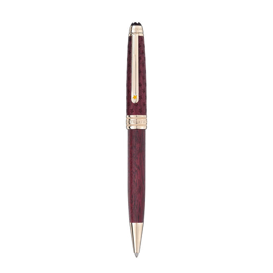 The Montblanc Meisterstuck Le Petit Prince and Planet Classique ballpoint pen exudes luxury with its polished, dark wood-like barrel and gold-colored accents, including the clip and tip. It is stylishly presented in a vertical position against a white background.