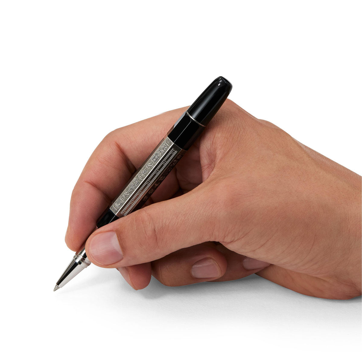 A hand holding a Montblanc Heritage Egyptomania Doue Rollerball Pen hovering above a blank surface, ready to write. The pen showcases an elegant silver and black design with a polished finish. The hand seems relaxed, fingers gently gripping the luxurious writing instrument from Montblanc.