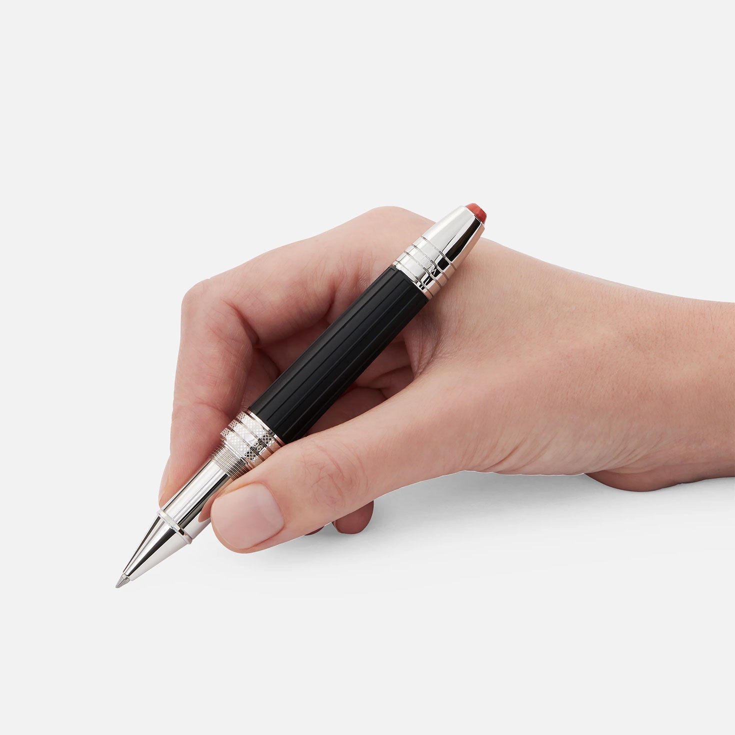 In a hand against a light gray background is the Montblanc Great Characters Jimi Hendrix Special Edition Rollerball Pen, featuring a sleek black and silver design. It showcases a silver clip and a striking red accent near the grip, reminiscent of an electric guitar's vibrant detail.