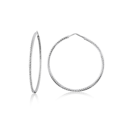 The Miss Mimi Medium Diamond Cut Sterling Silver Hoop Earrings by Miss Mimi by Yael are elegantly showcased on a white background. One earring is shown facing forward, and the other is turned to the side, accentuating their delicate, textured design. Crafted in Italy with precision, these hoops embody timeless beauty combined with modern style.