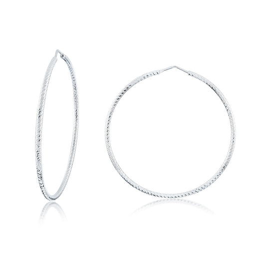 Introducing the Miss Mimi Large Diamond Cut Sterling Silver Hoop Earrings by Miss Mimi by Yael. These elegant, thin hoops feature a refined diamond-cut design and are crafted in Italy. One earring is depicted in profile while the other shows its face-on view, both accentuated beautifully by a reflective surface below.