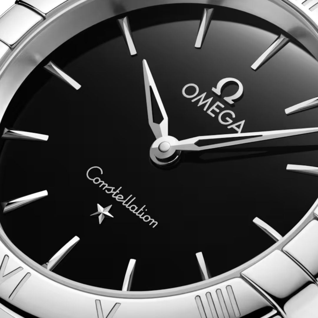 Close-up of the OMEGA Constellation Quartz 28mm Watch, featuring a black dial, silver hour markers and hands, the OMEGA logo, "Constellation" text, and a star above 6 o'clock on its stainless steel case.