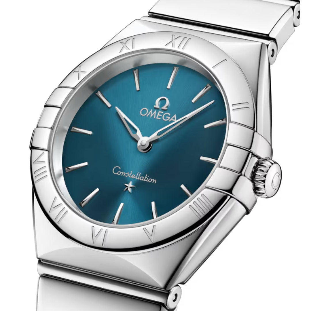 The OMEGA Constellation Quartz 28mm Watch features a stainless steel case, peacock blue dial, silver hour markers, Roman numeral bezel, and a sleek metal bracelet for a minimalist look.