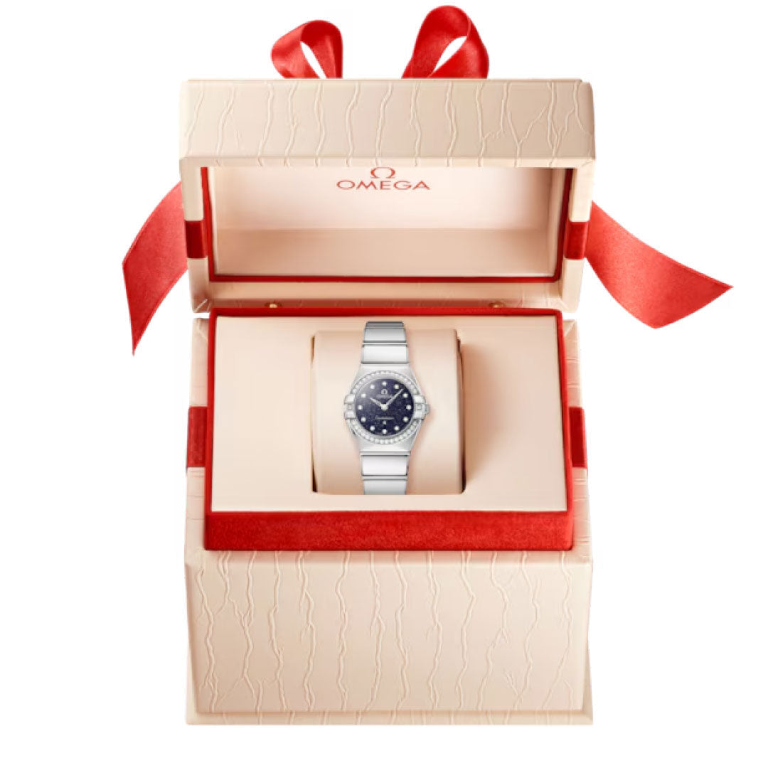 The OMEGA Constellation Quartz 25mm Watch is shown in an open cream-colored gift box with red accents and ribbon. The silver timepiece features a blue aventurine dial, with the OMEGA logo visible inside the box lid.
