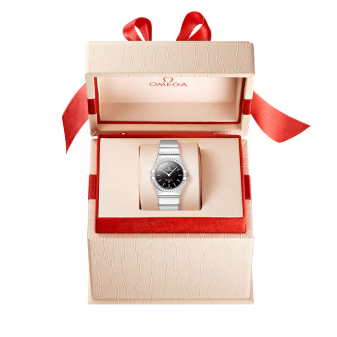 The OMEGA Constellation Quartz 28mm Watch by OMEGA, featuring a silver tone and black dial, is showcased in an elegant cream gift box with red lining and a red ribbon. The Omega logo appears inside the lid.
