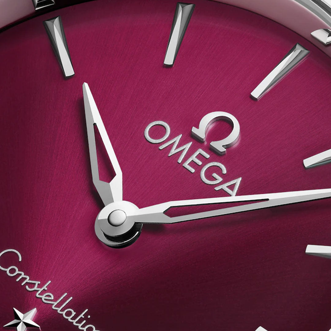 Close-up of the OMEGA Constellation Quartz 28mm Watch, featuring a red face, silver hands and markers, Omega logo, stainless steel case, and an elegant diamond-paved bezel.
