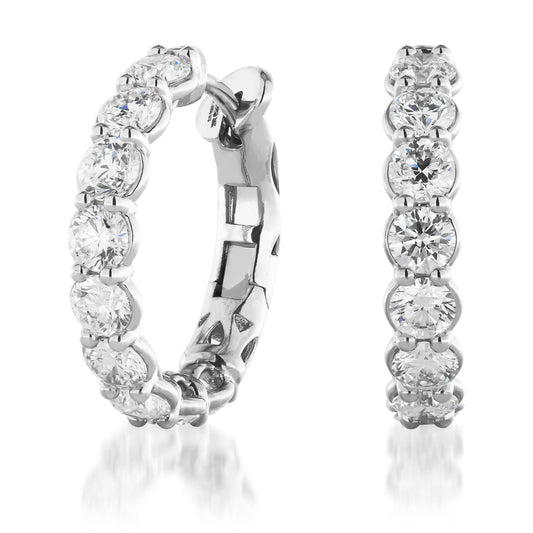 The Raffi&Co.® 14K White Gold Diamond Hoop Earrings are elegantly displayed, featuring round-cut diamonds set in lustrous white gold. Positioned to showcase both the front and side views, these earrings from Raffi&Co glisten beautifully on a reflective white surface.