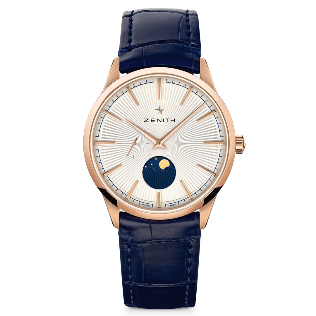 The ZENITH Elite Moonphase Elite 692 features a rose gold case, white dial, and blue alligator strap. It has slender markers, thin hands, and a moon phase at 6 o'clock with "Zenith" elegantly placed below the 12 o'clock marker.