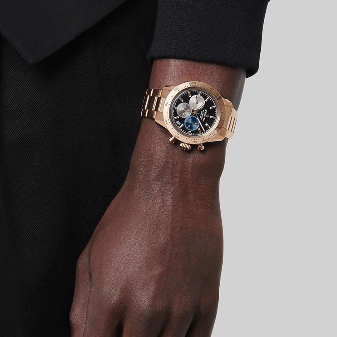 A person wears a ZENITH Chronomaster Sport El Primero 3600 41mm with a rose gold finish, featuring multiple subdials and a distinctive link bracelet. The black and white dial contrasts against their black clothing.