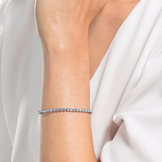A close-up of a person's arm adorned with the Swarovski Emily Tennis Bracelet. The person is dressed in an elegant white blouse, with their arm slightly bent and hand resting near their face. The minimalistic design of the bracelet catches the light, adding a touch of elegance.