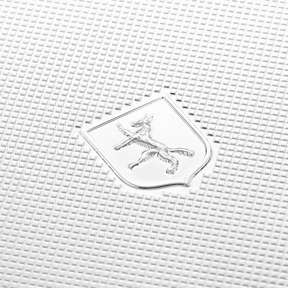 A close-up of an embossed emblem on a textured surface highlights a stylized animal, perhaps a lion or horse, rearing on its hind legs within a silver-plated shield. The background displays a grid pattern similar to the ultrasuede lining of the WOLF 1834 Silver Watch Jewellery and Legacy Box by WOLF.