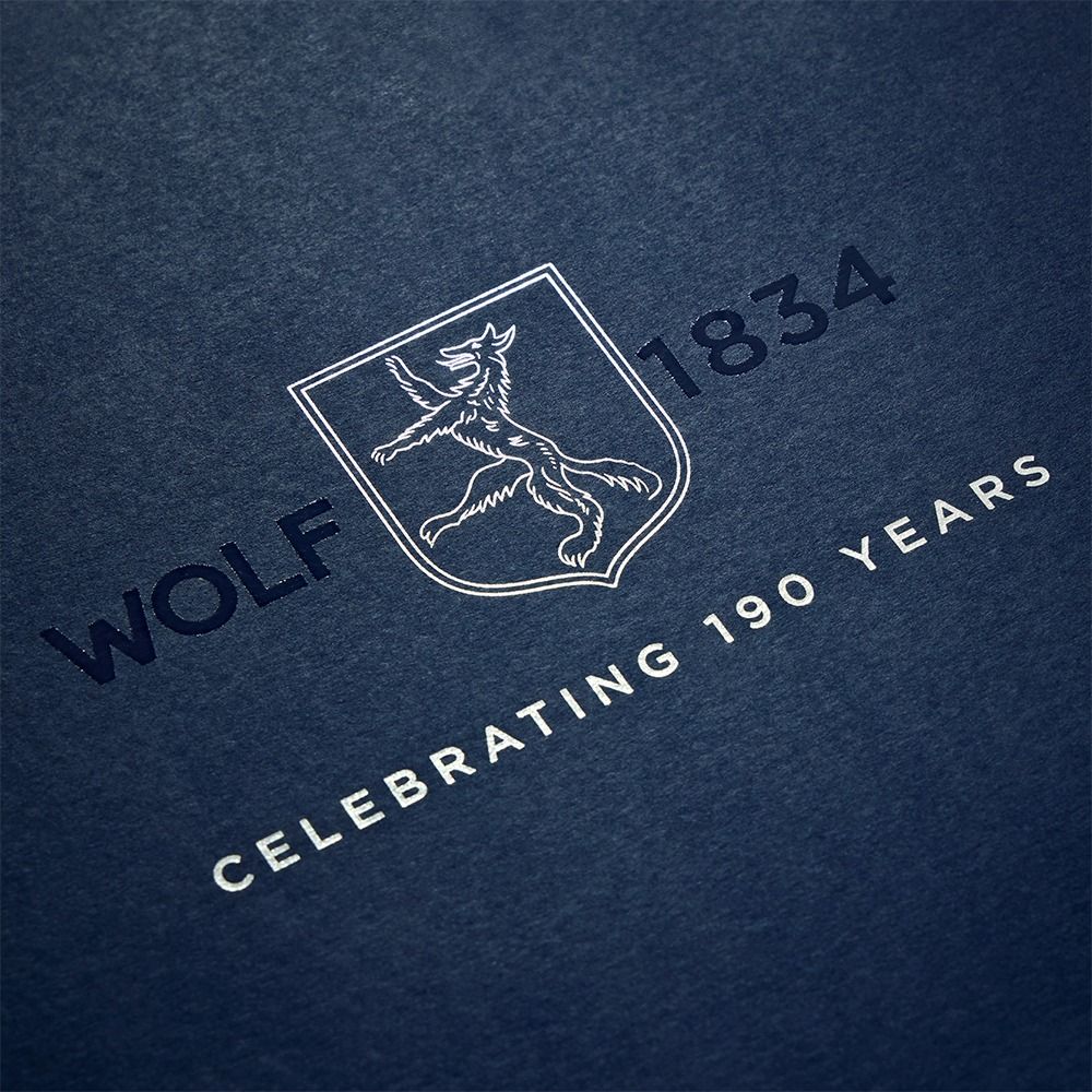 A blue background with a white crest featuring a wolf, the text “WOLF 1834,” and “CELEBRATING 190 YEARS” below, evoking the heritage of luxury timepiece accessories like the WOLF 1834 Single Watch Winder Silver from WOLF, renowned for its elegant craftsmanship.