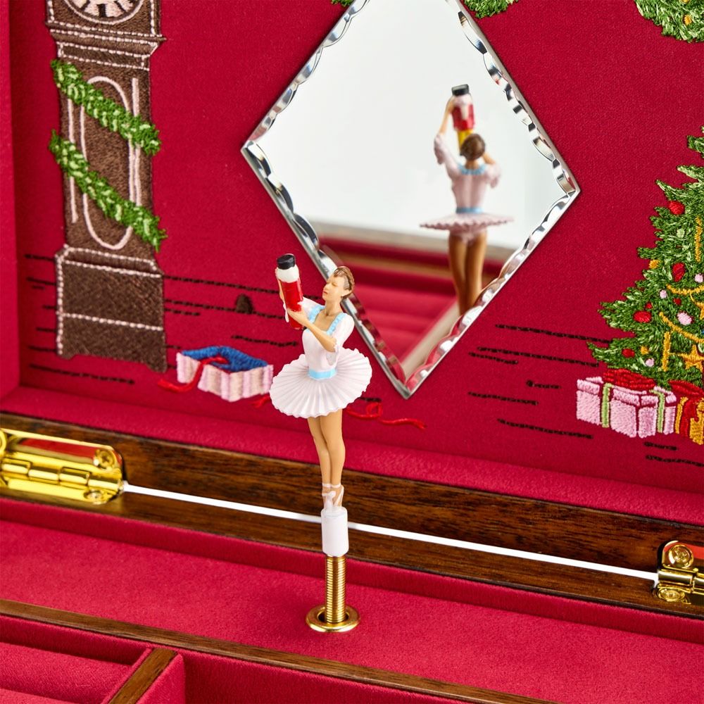 A ballerina figurine stands on a rotating base inside the WOLF 1834 Nutcracker Musical Box Jewelry Box Walnut, her graceful form mirrored on the lid. The elegant WOLF jewelry box is surrounded by festive Christmas decorations and wrapped presents in the background.
