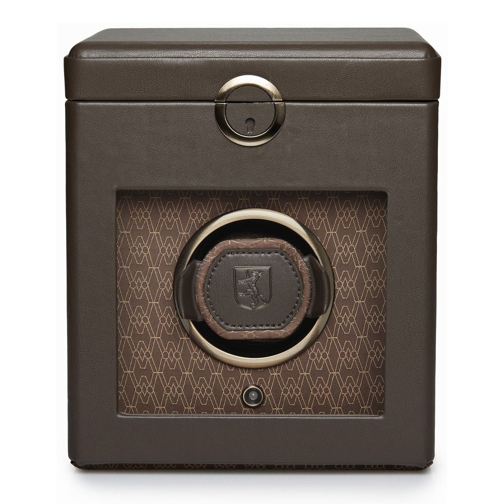 Introducing the WOLF 1834 Earth Single Watch Winder, a sophisticated accessory from the renowned brand WOLF. This Bluetooth-enabled watch winder features a rich brown leather exterior with luxurious metallic accents and a distinctive round logo at its center. The glass front display reveals a chic patterned interior alongside a circular compartment designed to securely hold your watch. Customize your experience with adjustable rotation settings for optimal performance.