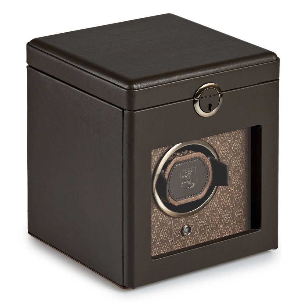 The WOLF 1834 Earth Single Watch Winder by WOLF is a brown leather cubic-shaped winder with a transparent front that beautifully displays your watch inside. It comes with a lockable lid and features patented innovation. The interior showcases a patterned design, while the watch is kept secure on a customizable rotation holder for precise timekeeping.