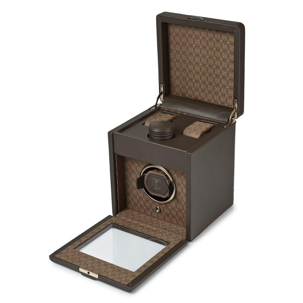 The WOLF 1834 Earth Single Watch Winder by WOLF is a luxurious brown accessory featuring a textured pattern and a transparent lid. It offers customizable rotation settings and showcases its patented design with a single watch slot. The open winder reveals an elegant interior design along with top-mounted controls.