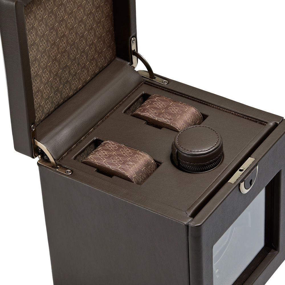 The WOLF 1834 Earth Single Watch Winder, offered by the brand WOLF, is designed in brown leather with an open lid. It features two cushioned compartments for watches and a round center compartment, all visible through a glass viewing panel. The winder offers customizable rotation settings and showcases a patterned brown interior that elegantly combines tradition with modern convenience.