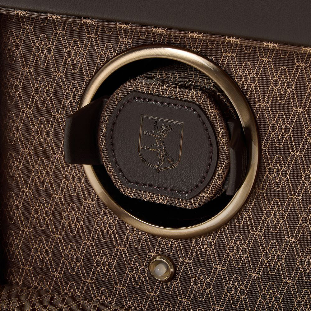 Close-up of the WOLF 1834 Earth Single Watch Winder's brown textured surface, featuring a geometric pattern and a metallic ring. Inside, discover a leather piece embossed with WOLF's iconic logo of an animal standing on its hind legs. Below, find a small round metallic button that is part of the patented Bluetooth watch winder functionality.