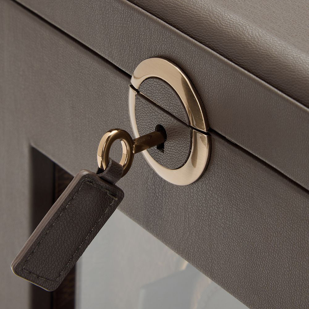 Close-up of the WOLF 1834 Earth Single Watch Winder, a brown leather case with a golden circular lock and inserted key, complete with a rectangular leather tag. This textured box showcases WOLF's patented innovation, offering the sophistication of a Bluetooth watch winder and customizable rotation to protect your valuables.