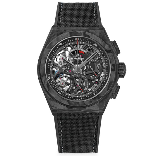 The Zenith Defy El Primero 21 44mm Watch features a black, partially skeletonized face with an automatic movement. It has a sleek carbon fiber case, textured strap, and reveals intricate cogs and gears accented in white and red over a plain white backdrop.