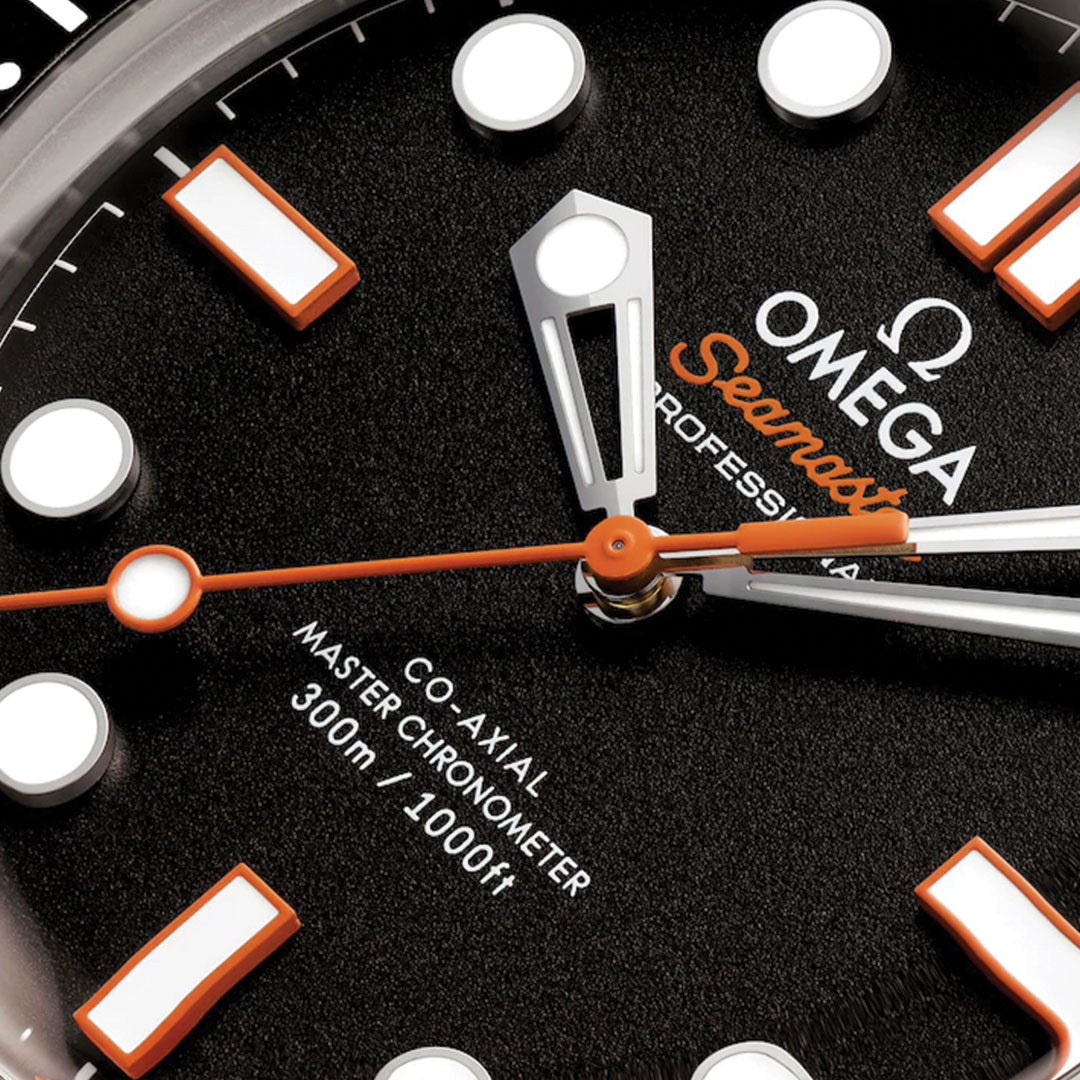 Close-up of the OMEGA Seamaster Diver 300M Co-Axial Master Chronometer 42mm watch face, with bold white hour markers, an orange second hand, and white hands on a black textured dial featuring OMEGA branding and depth rating.