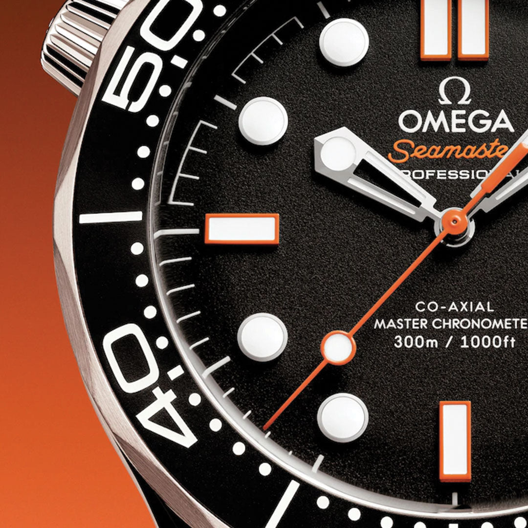 Close-up of the OMEGA Seamaster Diver 300M Co-Axial Master Chronometer 42mm, featuring a black dial with white and orange hour markers and hands. The watch’s bezel is partially visible against an orange-to-black gradient background.