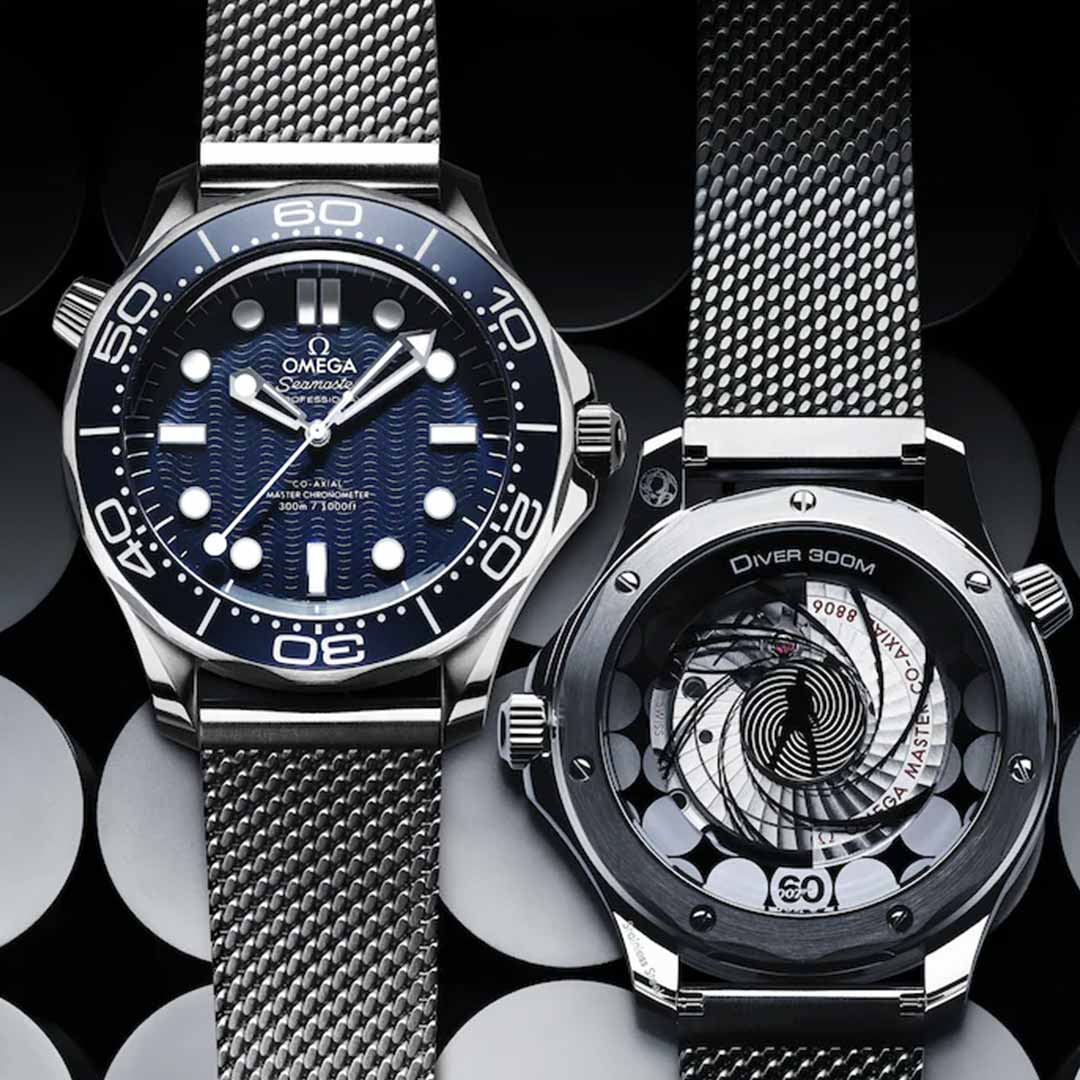 Two OMEGA Seamaster Diver 300M James Bond 60th Anniversary Co-Axial Master Chronometer 42mm Watches exude elegance. On the left, a blue dial with white markers and a silver bezel; on the right, a transparent case back reveals the intricate mechanics of the Master Chronometer Calibre 8806. Both feature metallic mesh straps, embodying the timeless allure of James Bond.