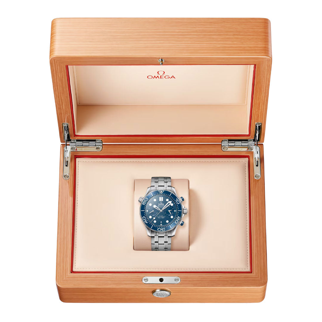 The OMEGA Seamaster Diver 300M Co-Axial Master Chronometer Chronograph 44mm watch, featuring a blue dial and bezel, is showcased in an open light wood box with a beige interior and the OMEGA logo inside the lid.