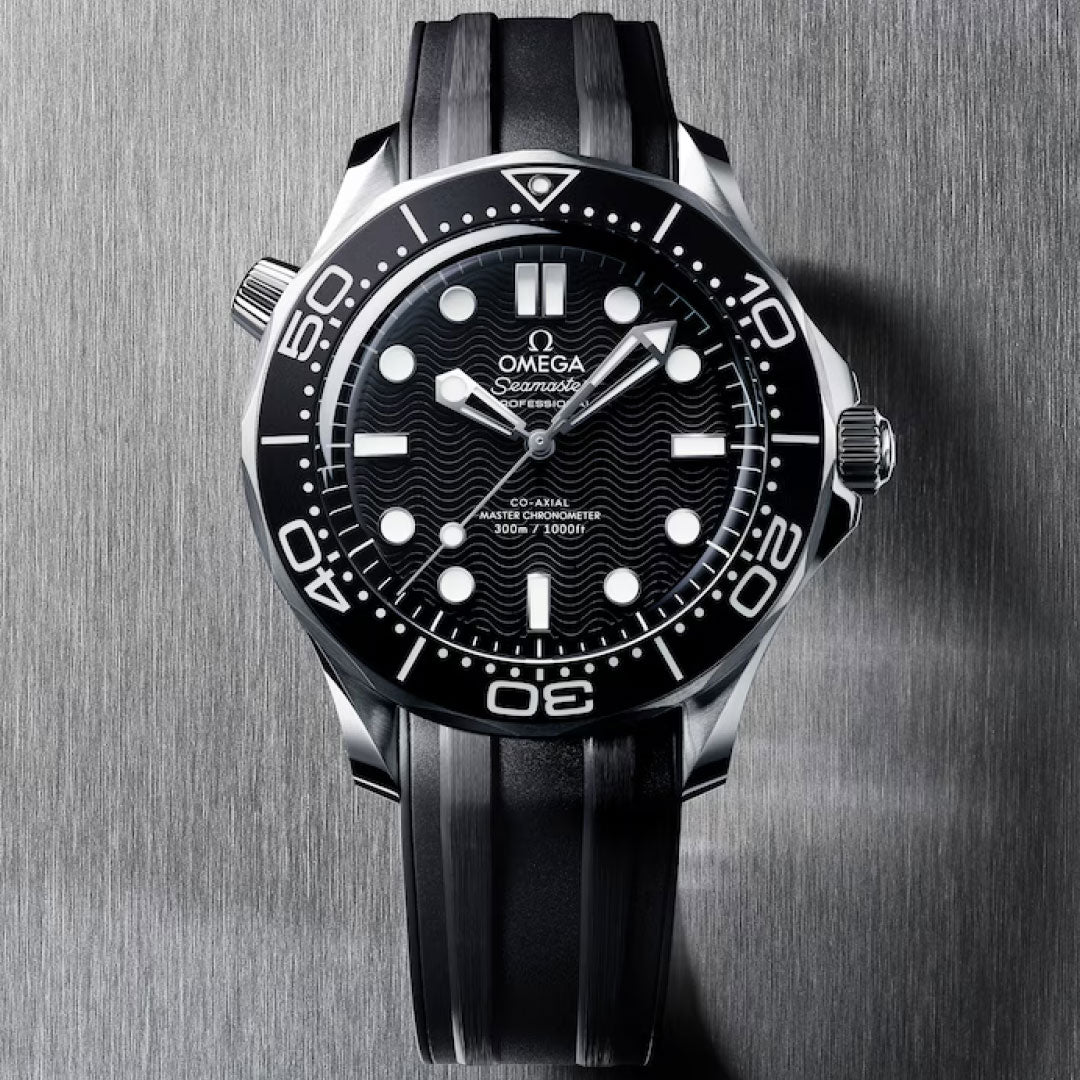 A close-up of the OMEGA Seamaster Diver 300M Co-Axial Master Chronometer 42mm Watch featuring a black dial, bold white hour markers, black rotating bezel, and rubber strap on a brushed metal surface.