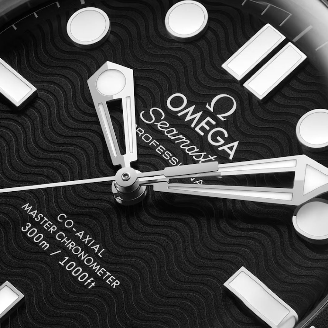 Close-up of the OMEGA Seamaster Diver 300M Co-Axial Master Chronometer 42mm watch face, featuring white Super-LumiNova hour markers, bold silver hands, a black wave-pattern dial, and "OMEGA Seamaster Professional" text.