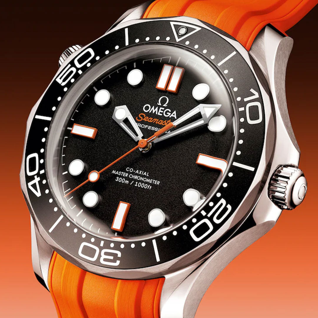 A close-up of the OMEGA Seamaster Diver 300M Co-Axial Master Chronometer 42mm Watch featuring a black dial with bold white hour markers, orange accents, a stainless steel case, and a bright orange rubber strap on an orange background.