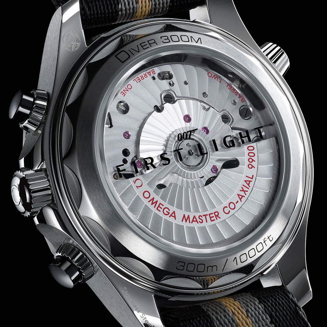 Close-up of the back of an OMEGA Seamaster Diver 300M 007 First Light Edition Co-Axial Master Chronometer Chronograph 44mm Watch, highlighting its intricate mechanical details, engravings, and the words “First Light,” “300m/1000ft,” and “Omega Master Co-Axial 9900.”.
