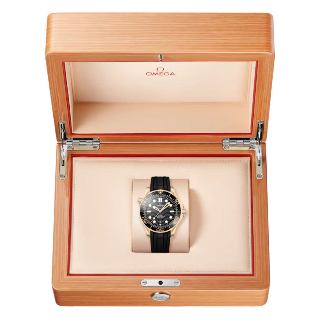 The OMEGA Seamaster Diver 300M Co-Axial Master Chronometer 42mm Watch in 18K Moonshine™ Gold with a black strap is presented in a beige-lined wooden box featuring the OMEGA logo inside the lid.