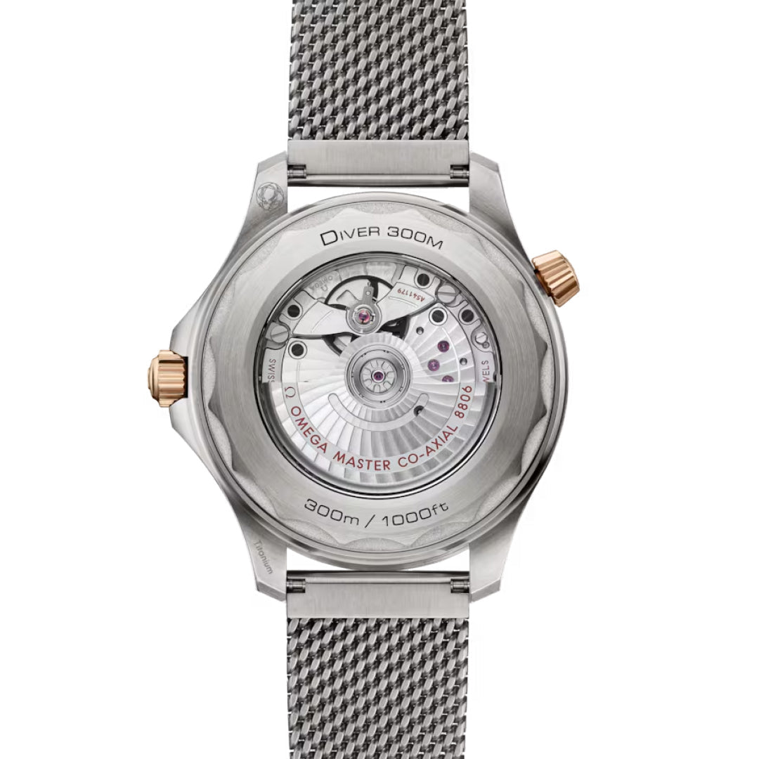 The image shows the back view of the OMEGA Seamaster Diver 300M Co-Axial Master Chronometer 42mm, highlighting its intricate mechanism. It features a metal mesh strap, gold accents, "Diver 300M" script, and ensures precision with its OMEGA Co-Axial Master Chronometer movement.