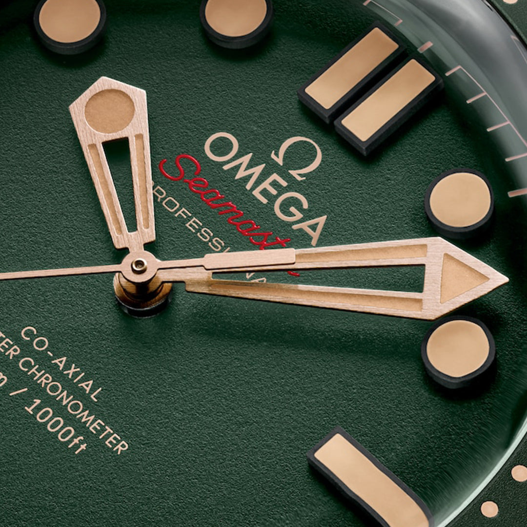 A close-up of the OMEGA Seamaster Diver 300M Co-Axial Master Chronometer 42mm watch face shows gold hour markers and hands, a red "Seamaster," "Professional" below, depth markings on the outer edge, and Co-Axial Master Chronometer tech on the left for enhanced precision.